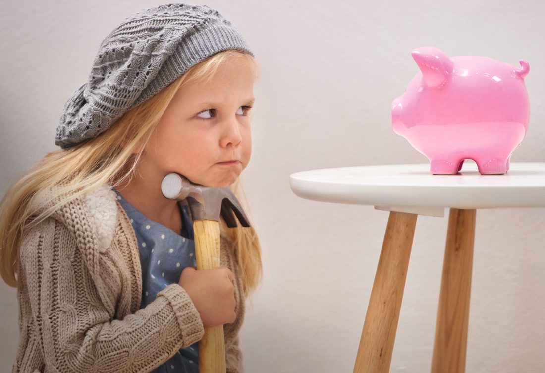 To break or not to break. A cute girl with a hammer eyeing her piggy bank.